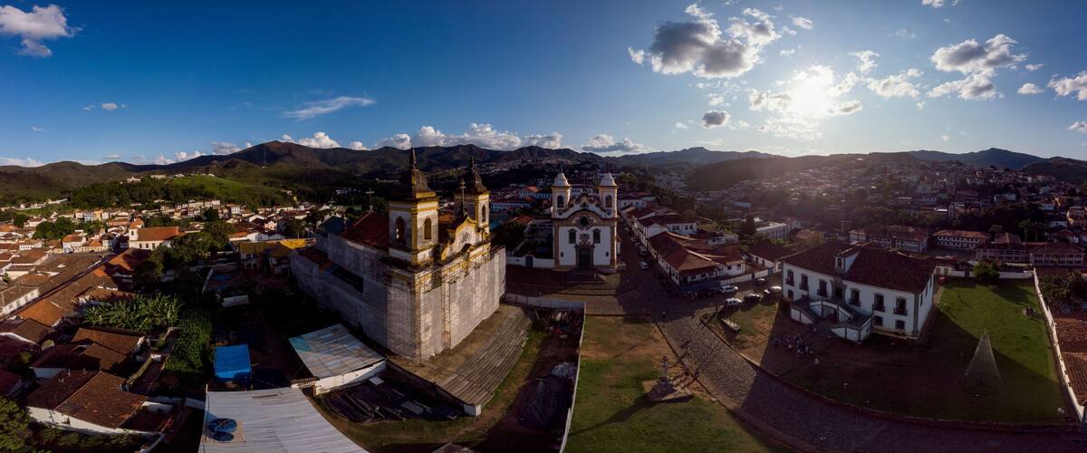 A cathedral with two towers, surrounded by a town with red-roofed buildings and a mountainous backdrop.