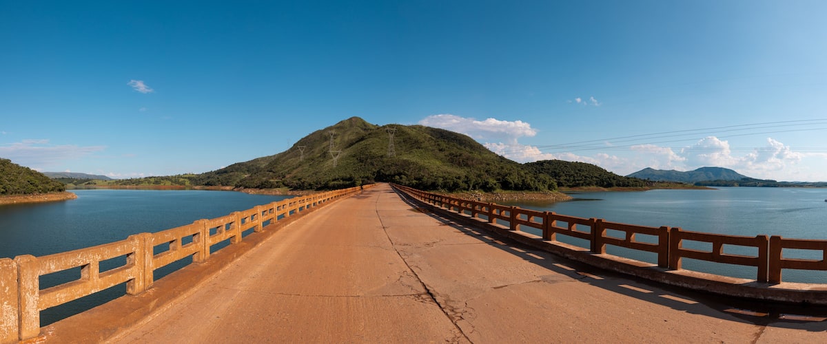 A bridge over a calm lake with a forested hill in the background.