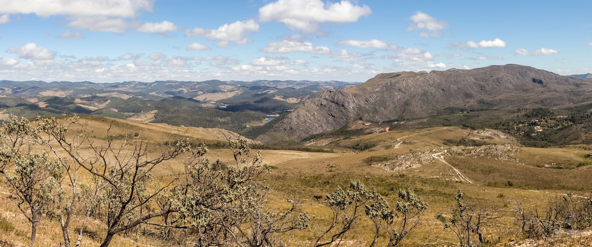 A mountainous landscape with rolling hills, sparse vegetation, and a clear sky.