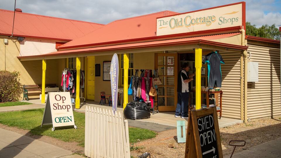 The Old Cottage Shops with a red roof, a yellow awning, and various items displayed outside.