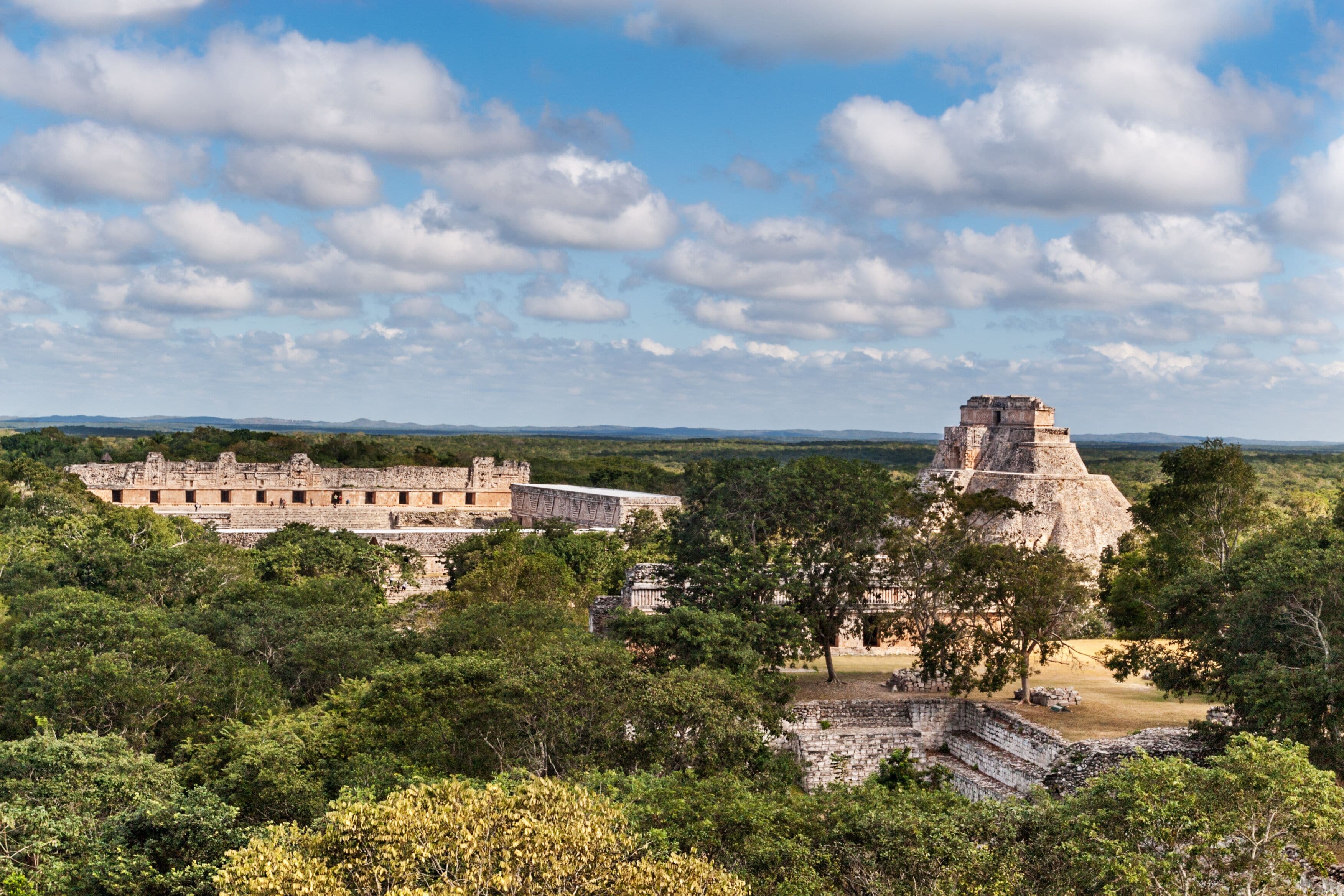 A Mayan ruin with large stone structures and a pyramid, surrounded by dense forest.