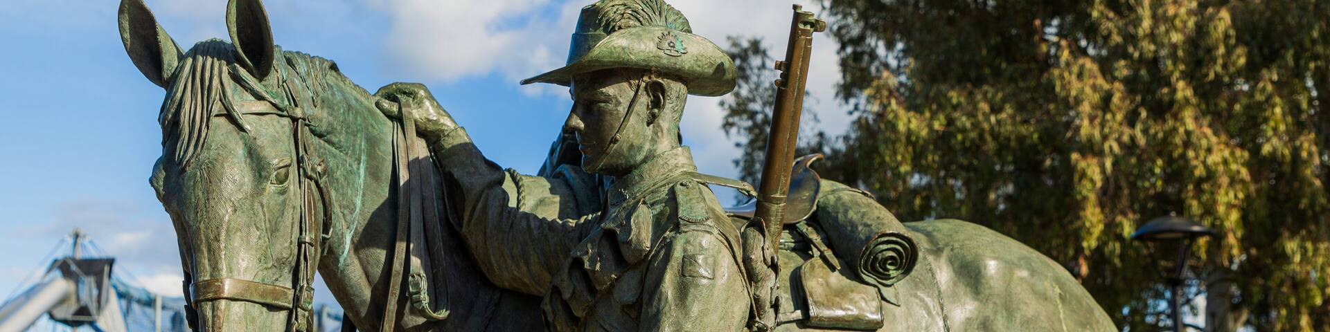 A bronze statue of a mounted figure with a horse in a park.