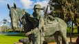 Una estatua de bronce muestra una figura a caballo en un parque.