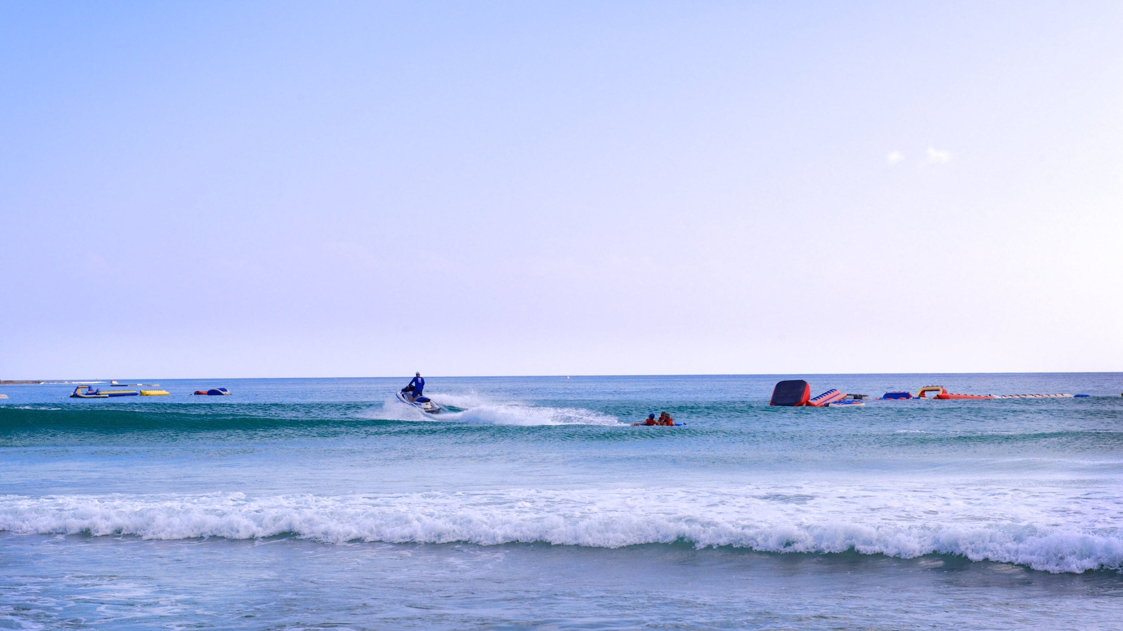 A beach with waves, a person on a jet ski, and several boats in the water.