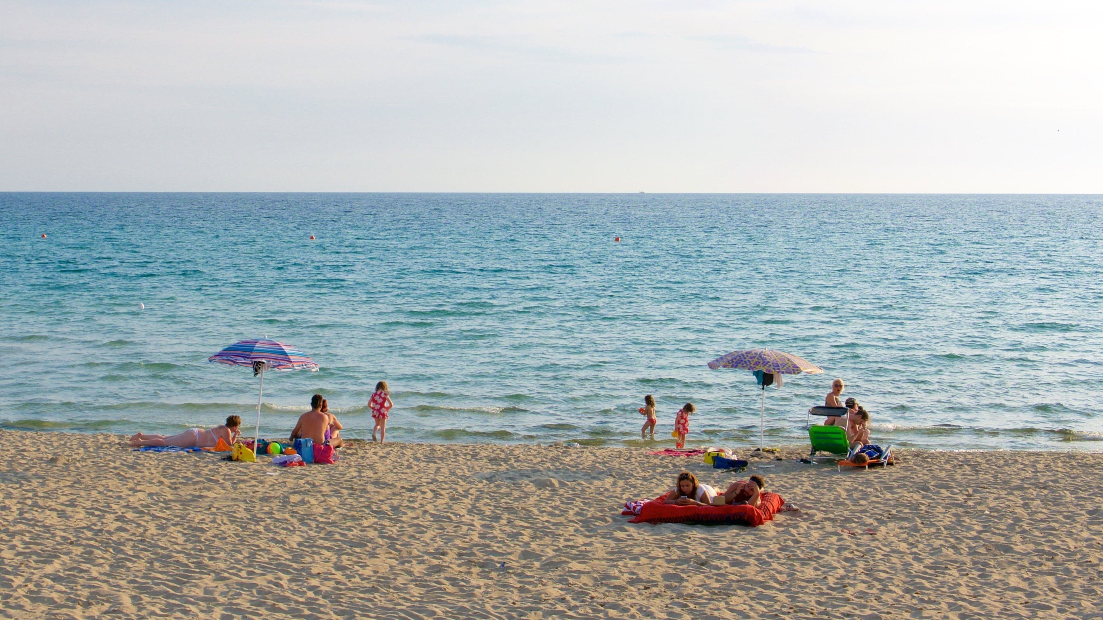 A sandy beach with people relaxing and playing near the water.