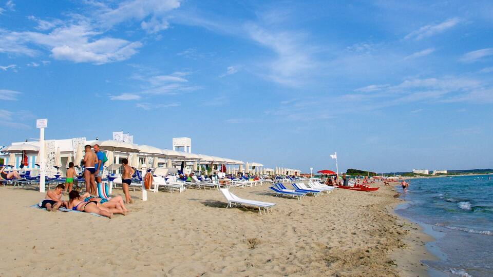 A beach with sun loungers and umbrellas, a boat, and a clear blue sky.