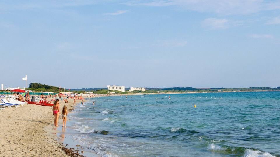 A beach with people, umbrellas, and buildings in the background.