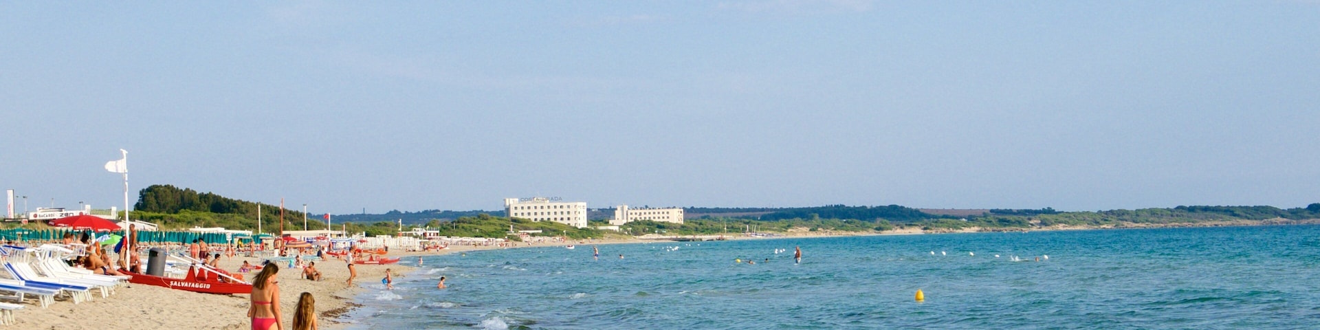 Una playa con gente, sombrillas y edificios al fondo.