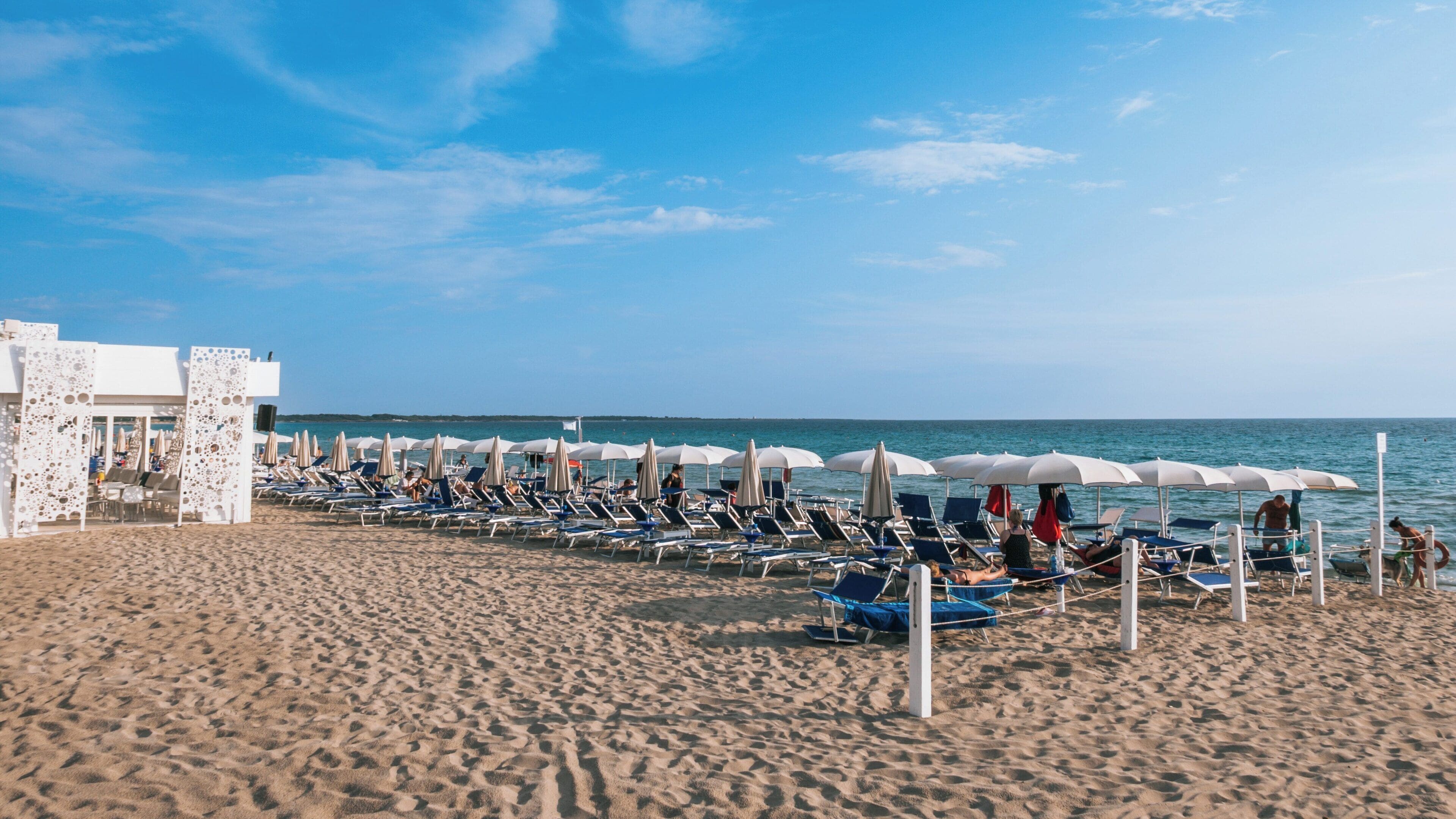 Relaxing atmosphere at Baia Verde Beach in Gallipoli, Puglia, Italy with sun loungers and umbrellas under a clear blue sky