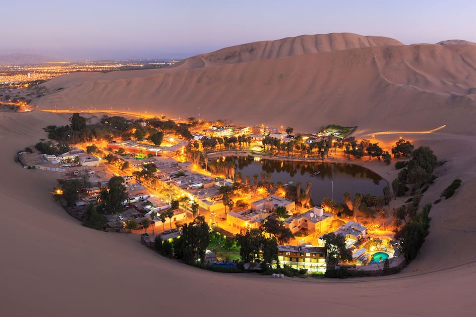 A desert settlement with a central water body, surrounded by sand dunes.