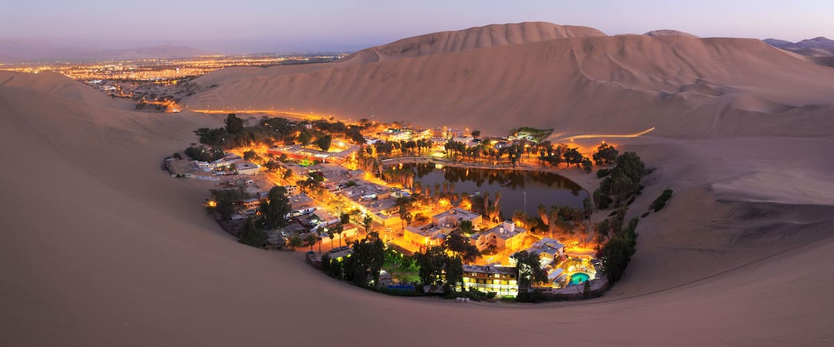A desert settlement with a central water body, surrounded by sand dunes.