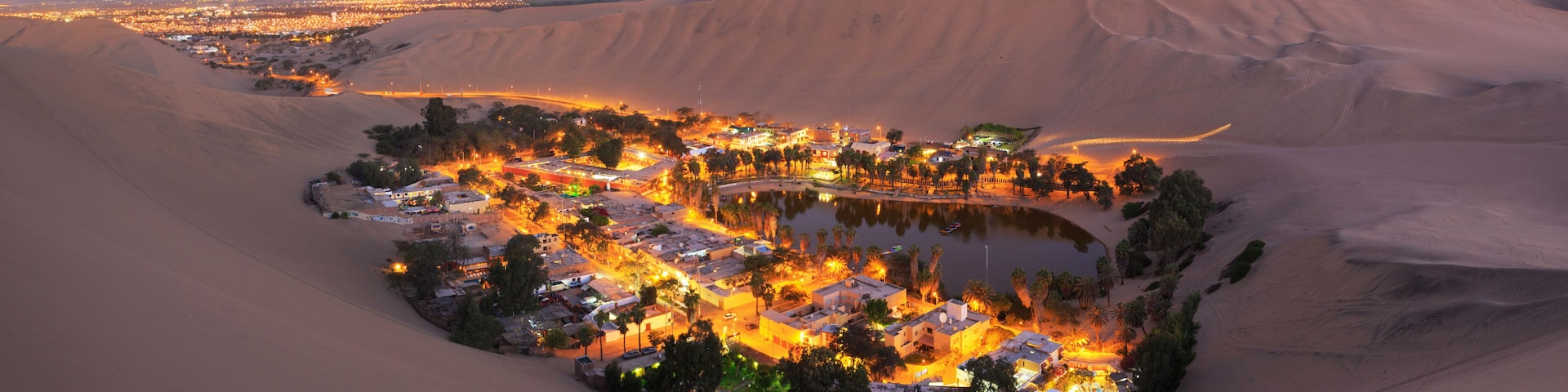 A desert settlement with a central water body, surrounded by sand dunes.