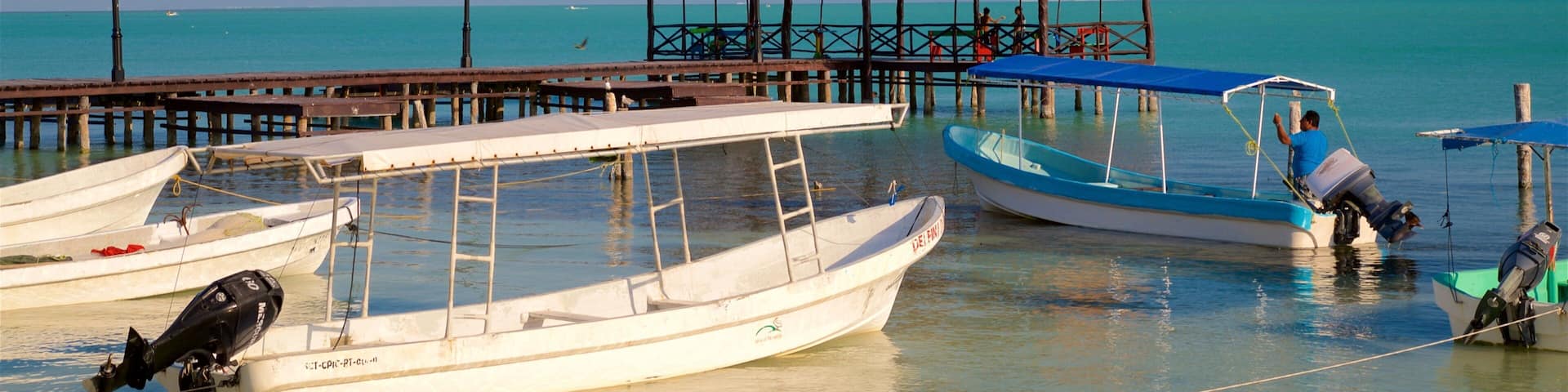 A pier with several boats docked, a thatched-roof structure, and a clear blue sea.
