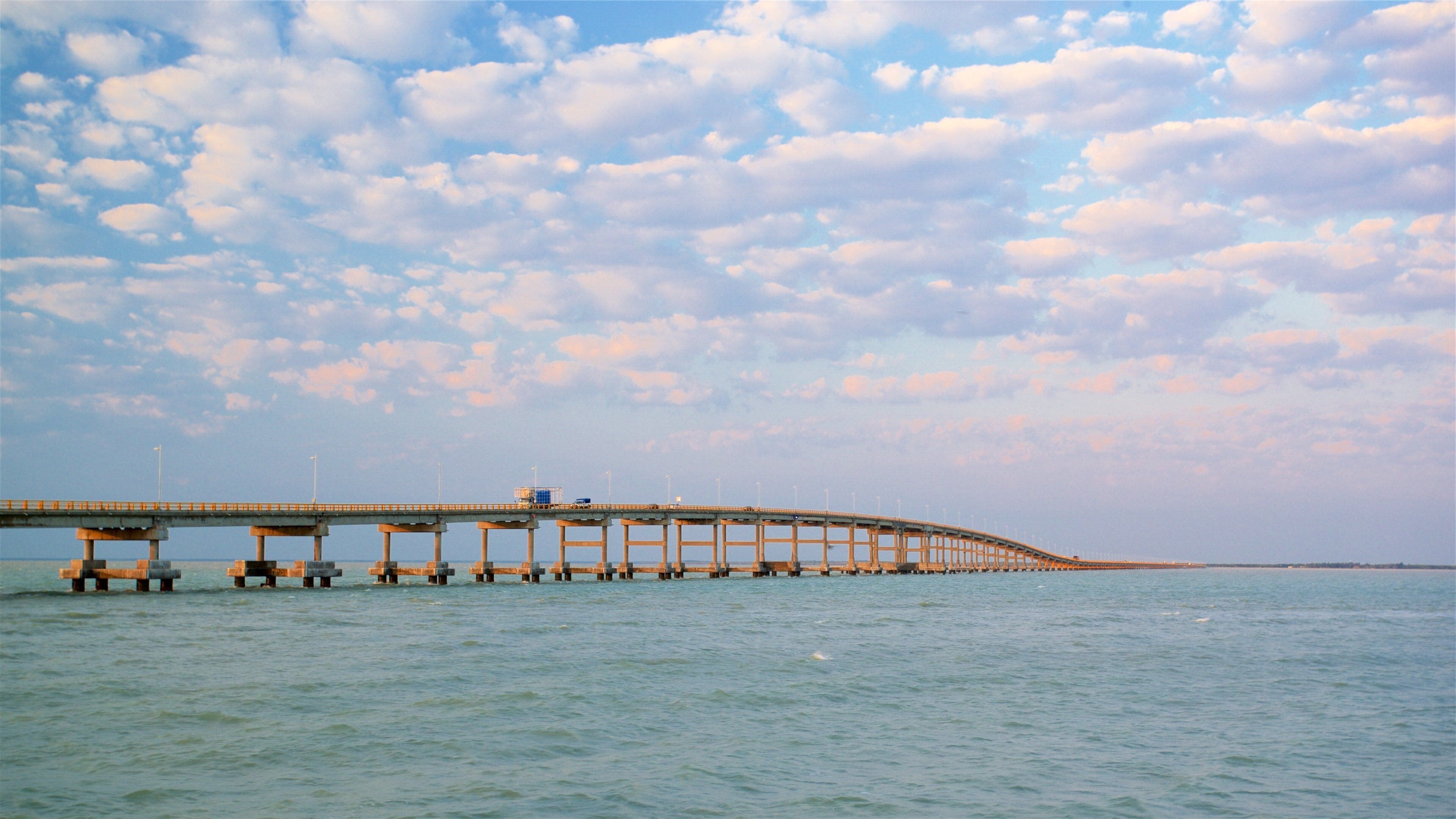 A long bridge over calm water under a partly cloudy sky.
