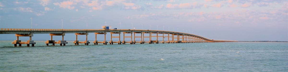 A long bridge over calm water under a partly cloudy sky.