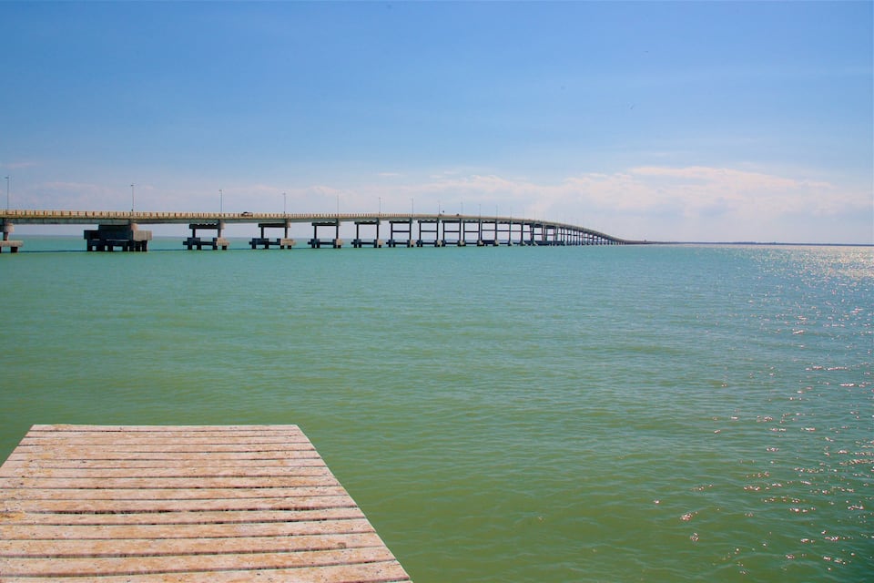 A wooden pier extending into calm waters, leading to a long bridge with multiple supports.