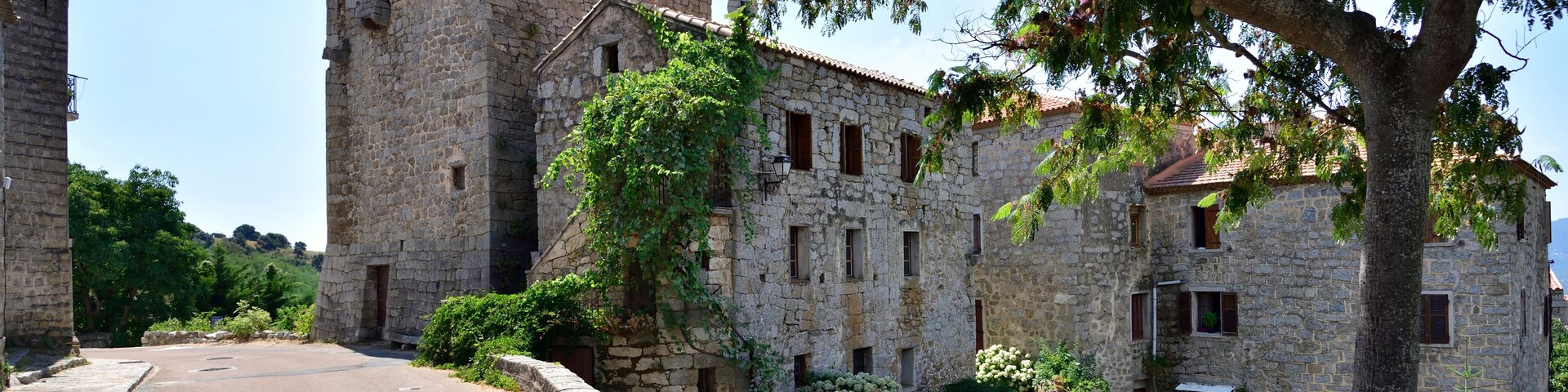 A stone building with a tower, surrounded by trees and a paved road.