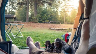 A person relaxing in a tent with a view of a grassy area and trees.