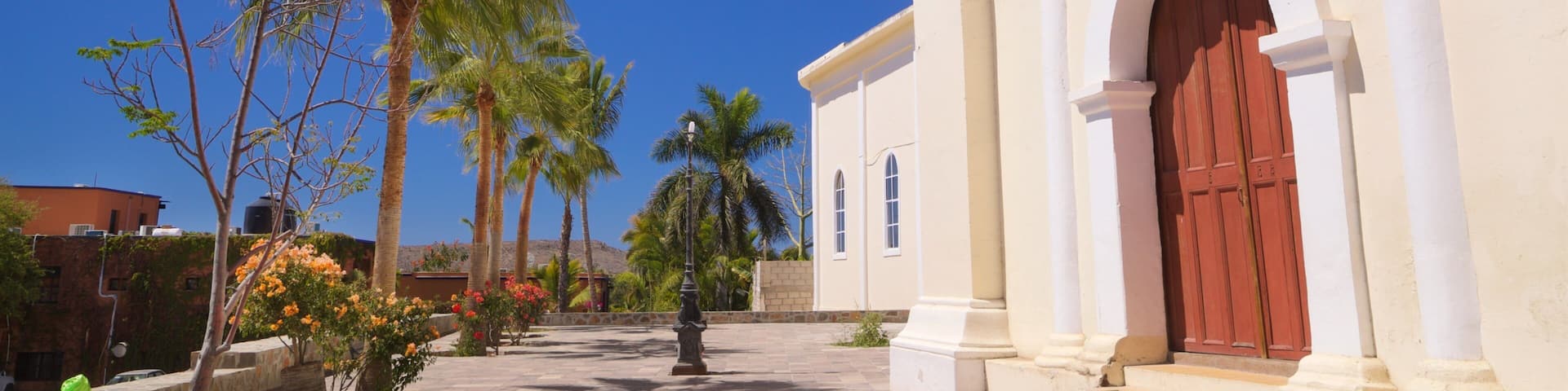 A colonial-style building with a red door, palm trees, and a clear blue sky.