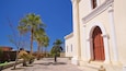 A colonial-style building with a red door, palm trees, and a clear blue sky.