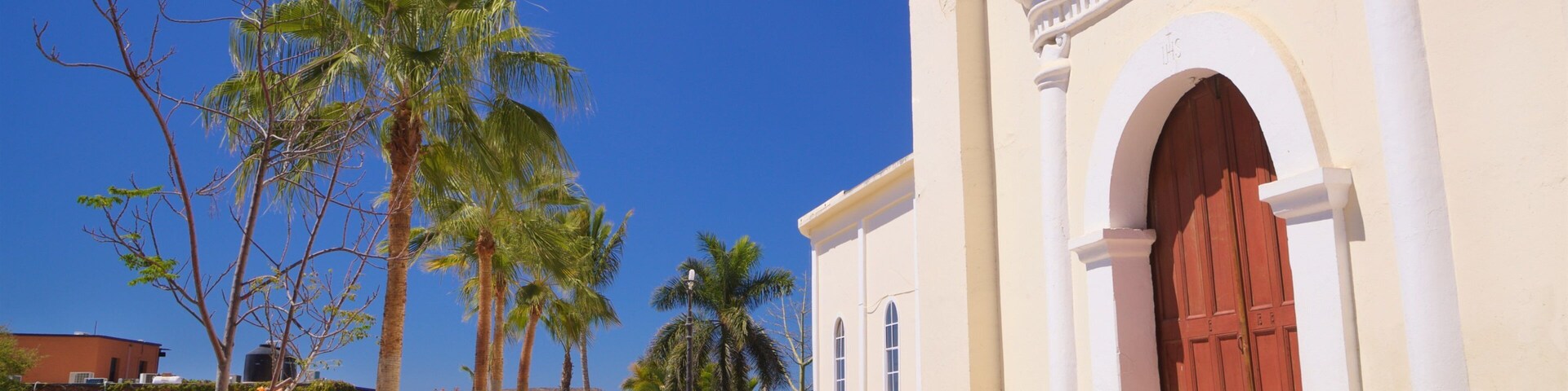 Um edifício em estilo colonial com porta vermelha, palmeiras e um céu azul claro.