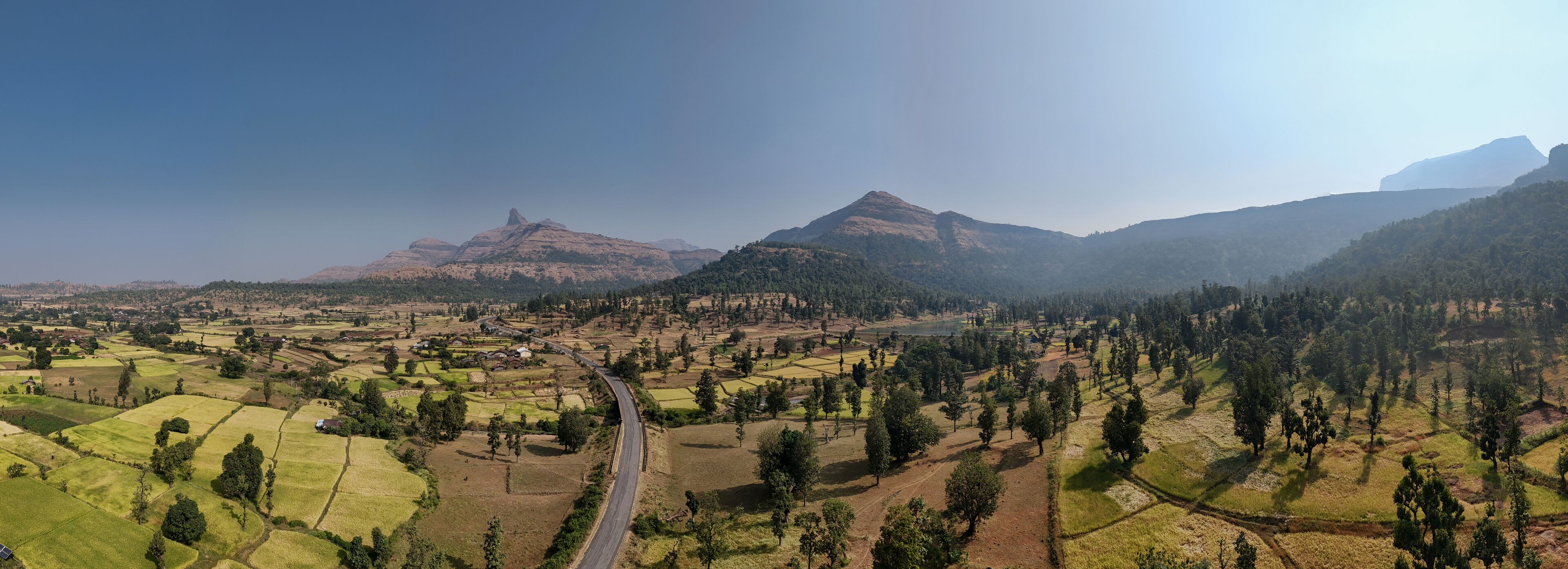 A rural landscape with terraced fields, a winding road, and mountains in the background.