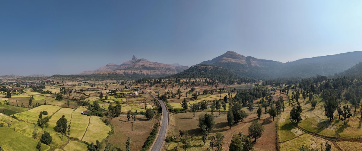 A rural landscape with terraced fields, a winding road, and mountains in the background.