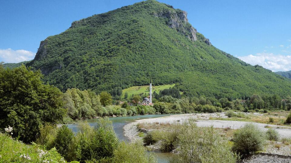 A river flowing through a valley with a prominent green hill in the background.