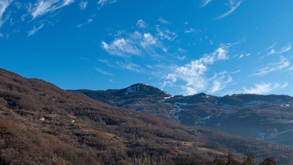 A mountainous landscape with a clear blue sky and scattered clouds.