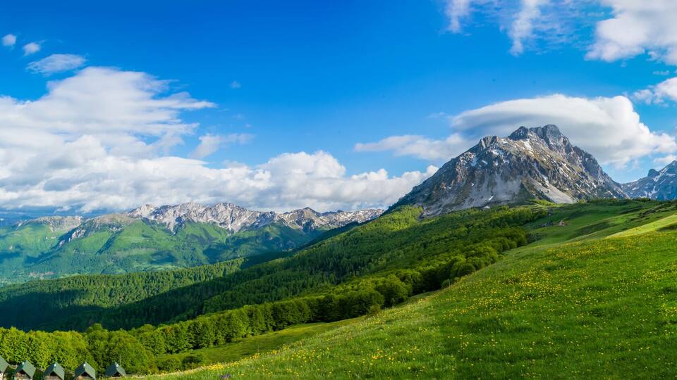 A mountainous landscape with a prominent peak, lush green valleys, and scattered houses.