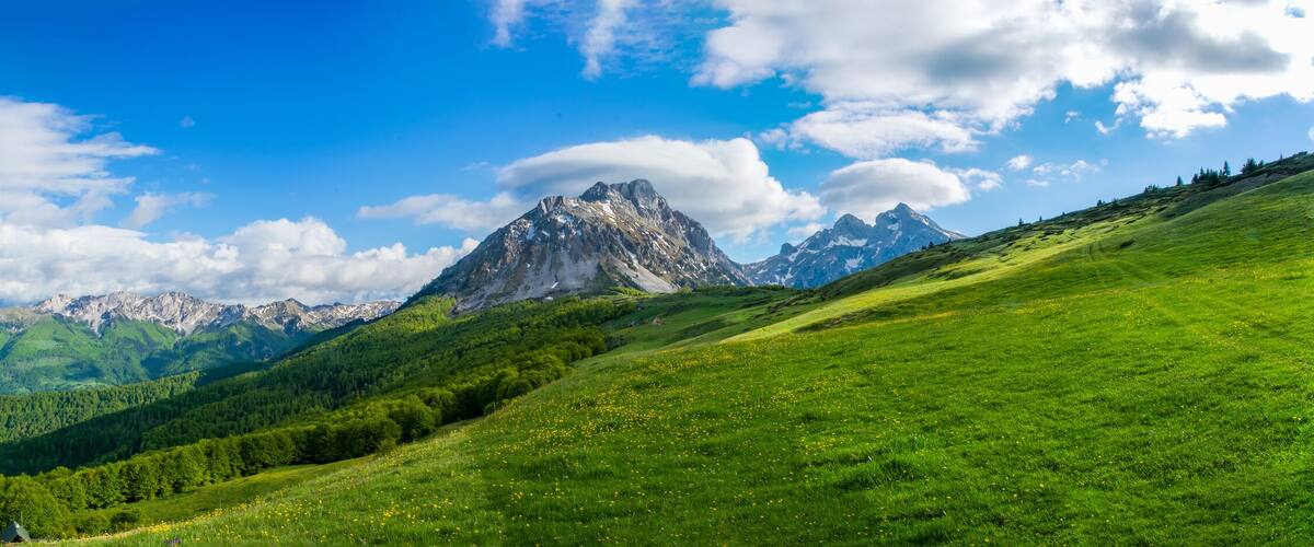 A mountainous landscape with a prominent peak, lush green valleys, and scattered houses.