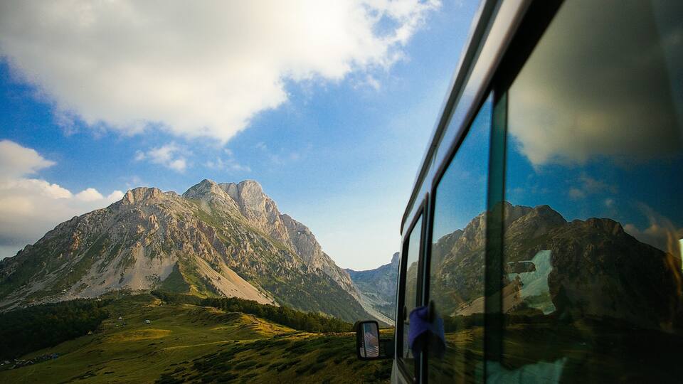A mountainous landscape with a vehicle window reflecting the scenery.