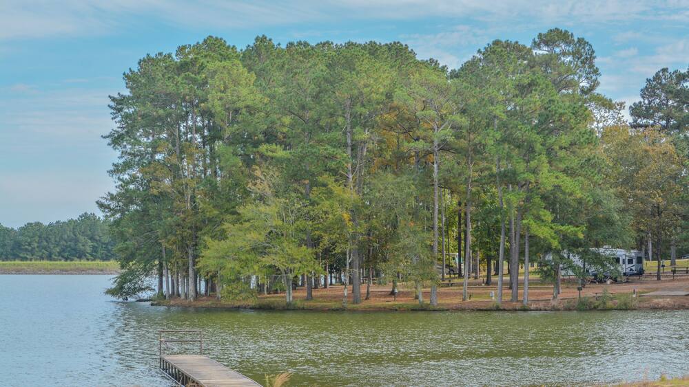 A lake with a dock, surrounded by trees and a RV park.