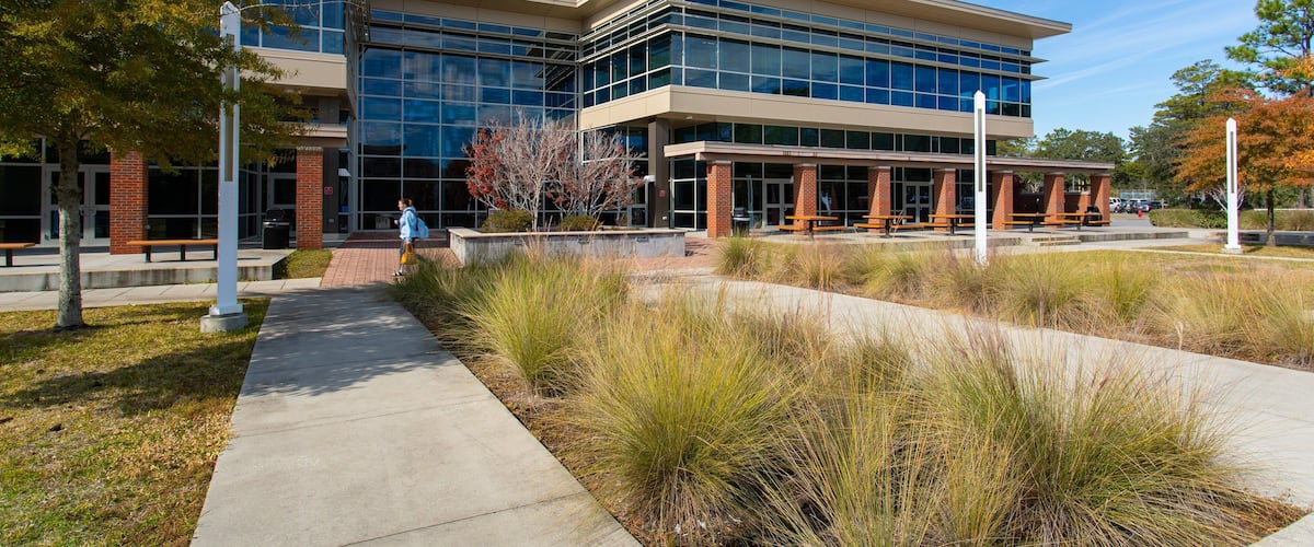 A modern building with glass windows and brick pillars, surrounded by a landscaped area with pathways and benches.