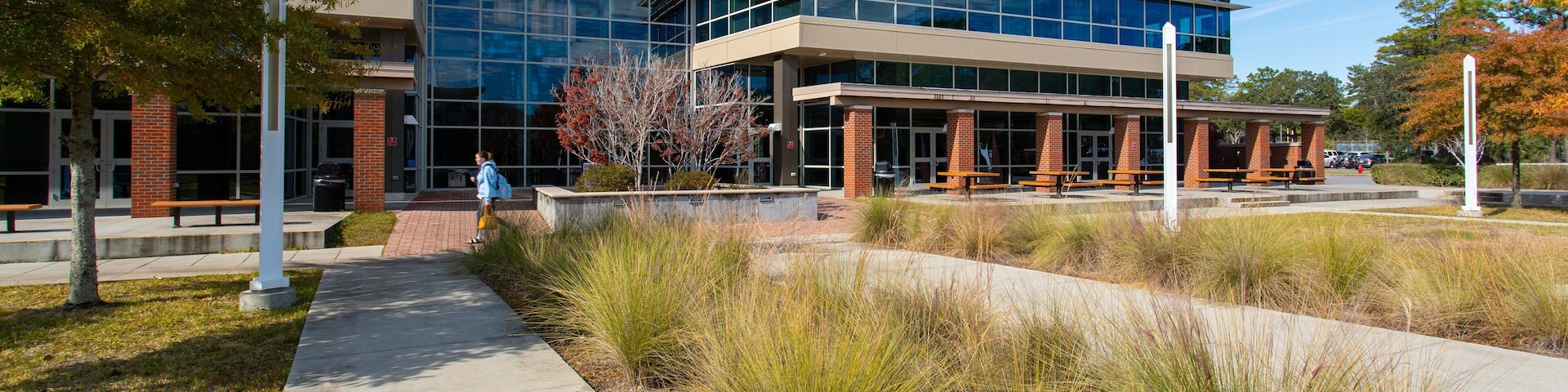 A modern building with glass windows and brick pillars, surrounded by a landscaped area with pathways and benches.