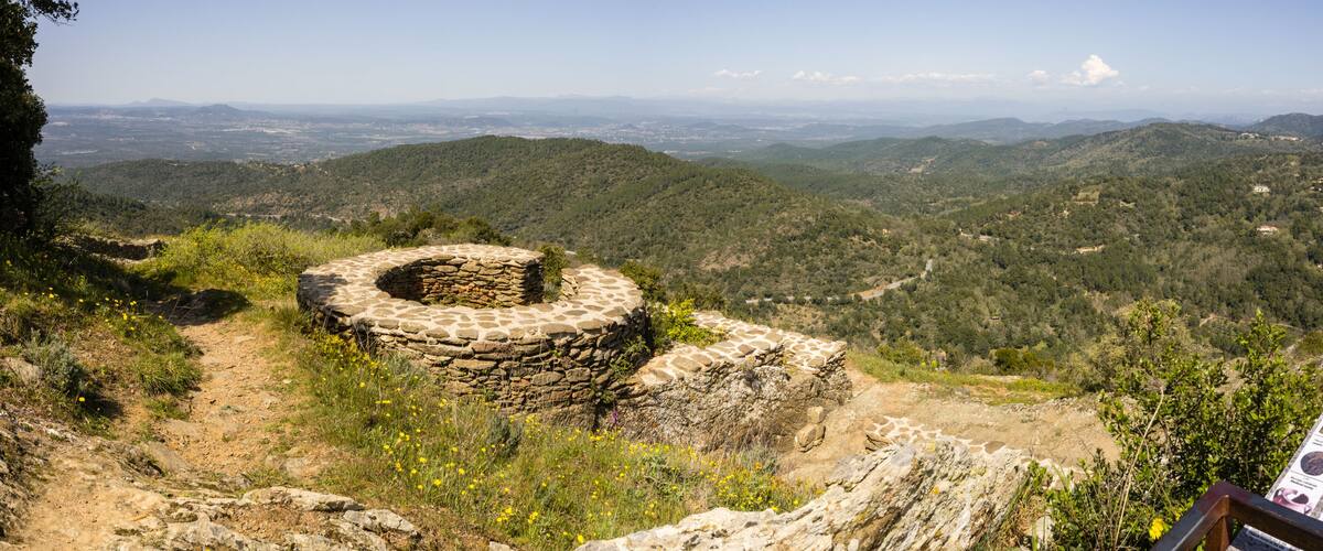 A stone structure on a hillside with a panoramic view of distant mountains and valleys.