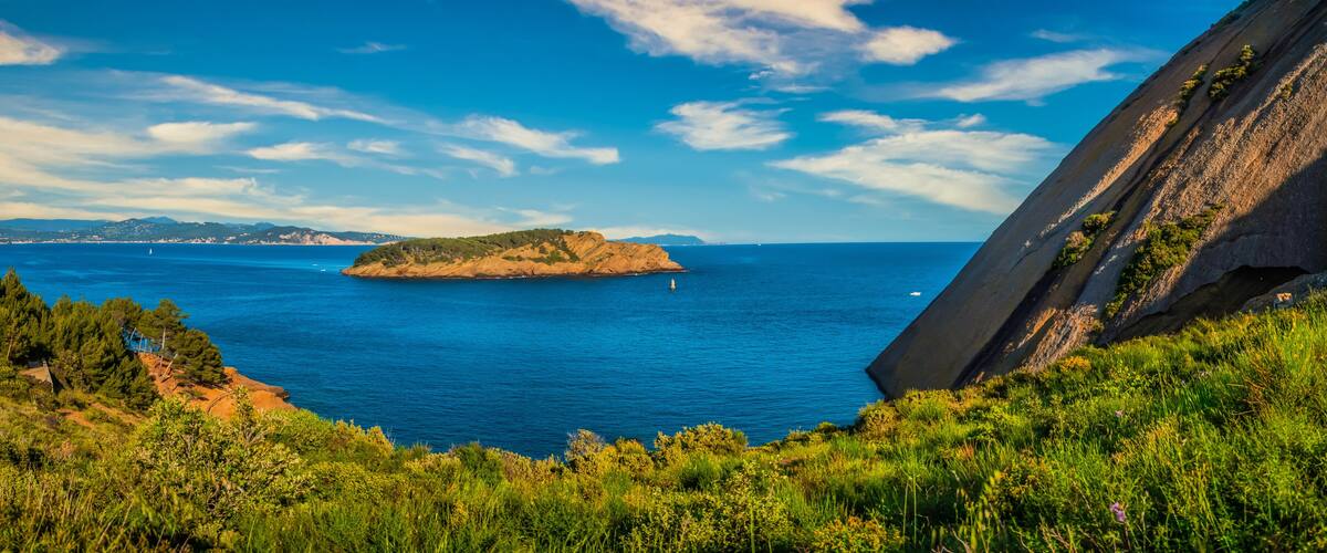 A coastal landscape with a prominent rock formation, a small island, and a clear blue sea.