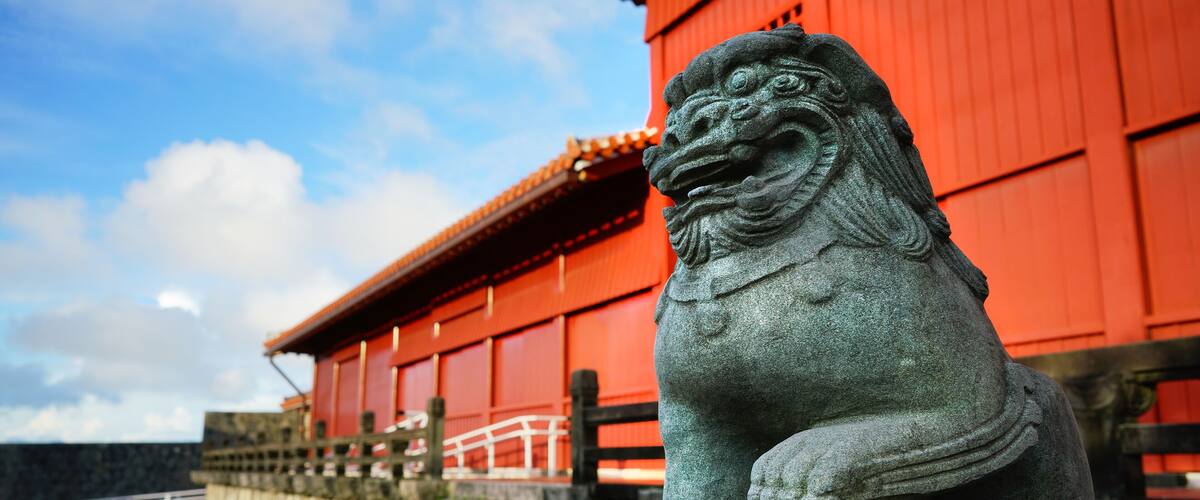 A stone lion statue in front of a red building with a traditional roof.