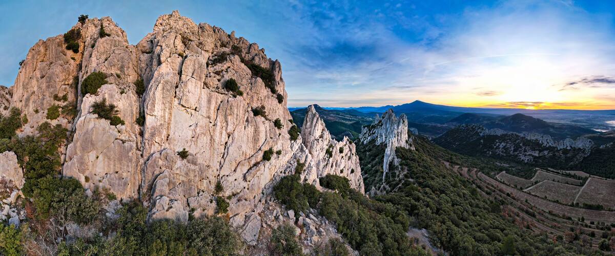 A rugged mountain landscape with prominent rock formations and terraced vineyards.