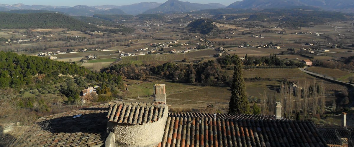 A rural landscape with terraced fields, a prominent mountain range, and scattered buildings.