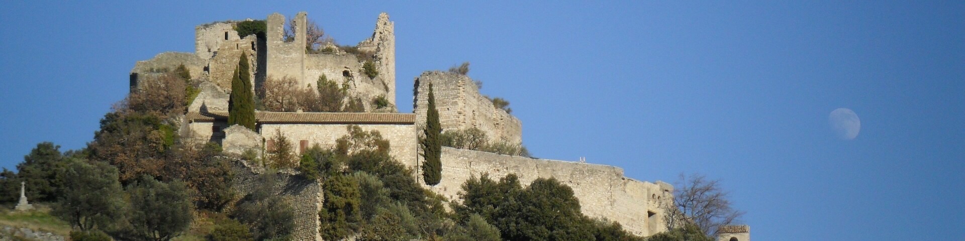 Un castillo histórico en una colina, bajo un cielo despejado y con la luna visible.