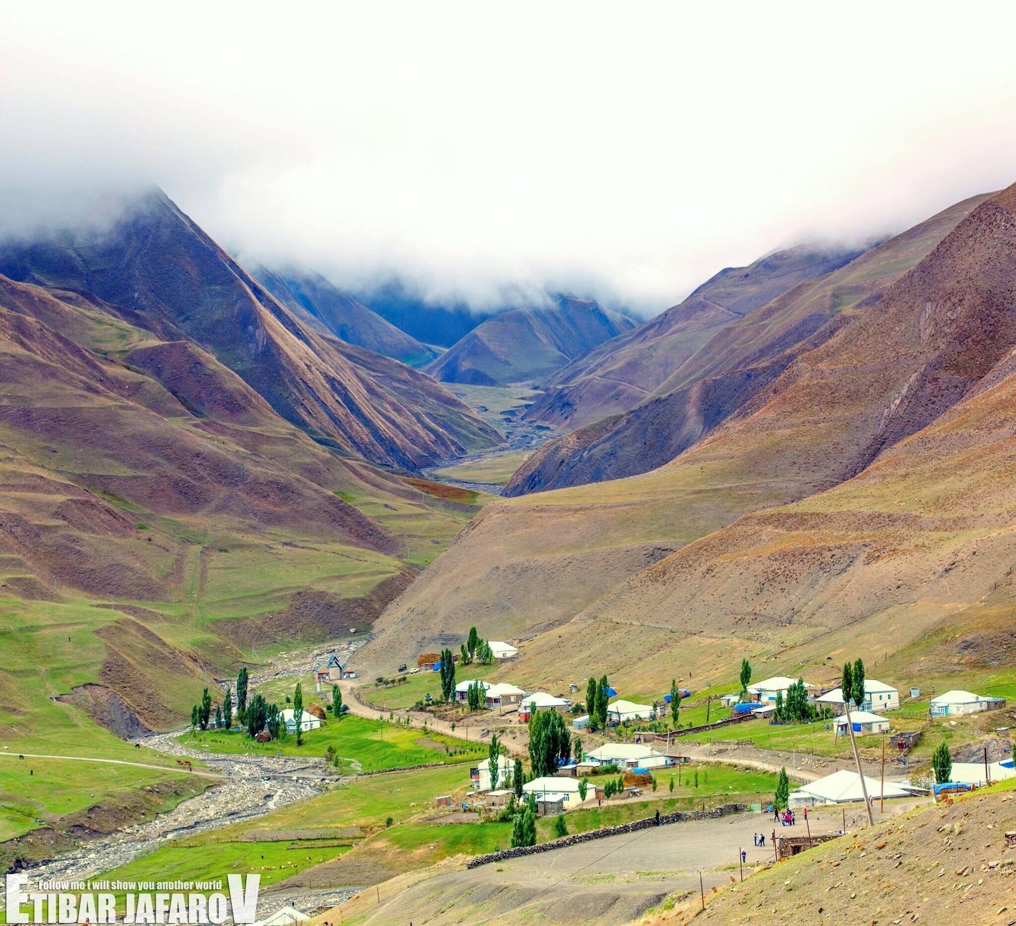 A mountainous landscape with a valley, houses, and a river.