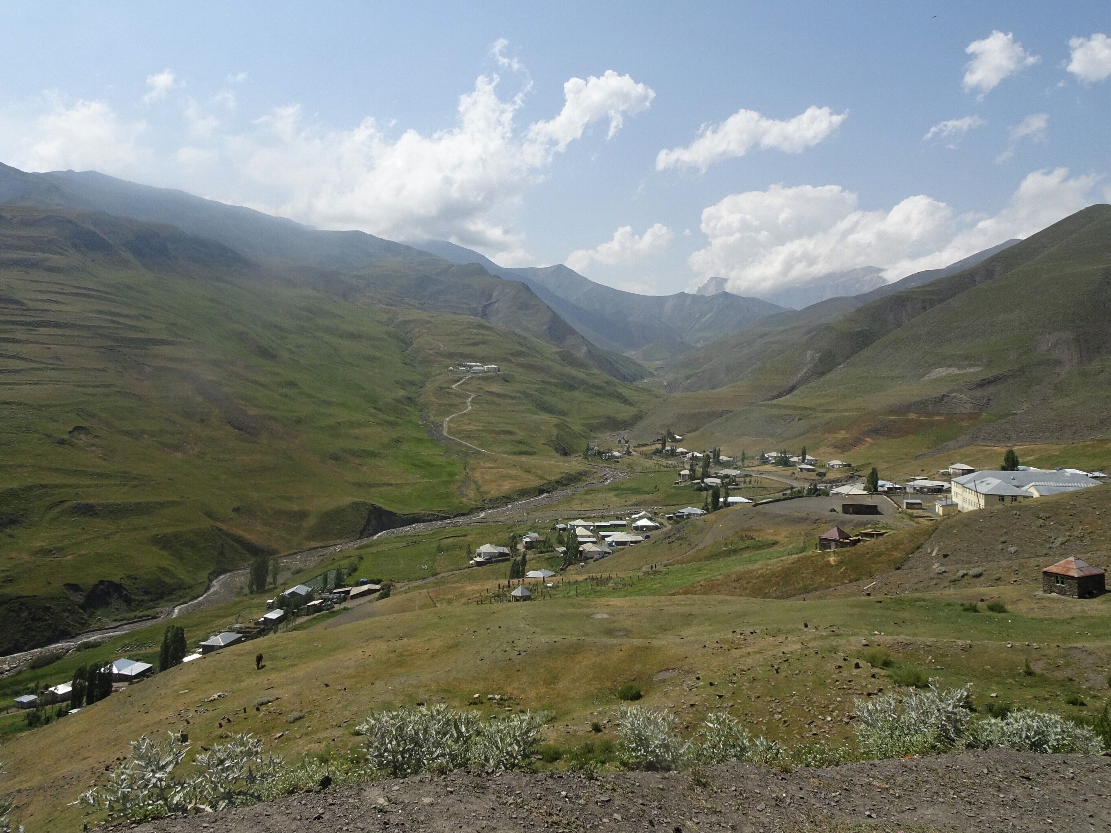 A valley with a small settlement, green hills, and distant mountains.