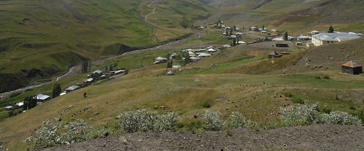 A valley with a small settlement, green hills, and distant mountains.