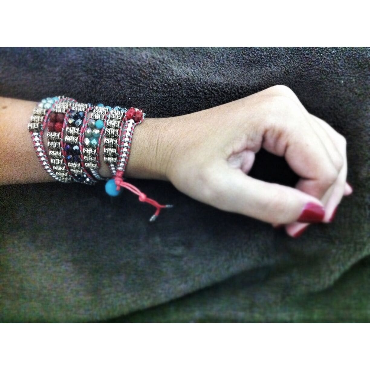 A hand with multiple bracelets, including a prominent red and silver one.