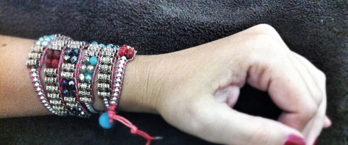A hand with multiple bracelets, including a prominent red and silver one.