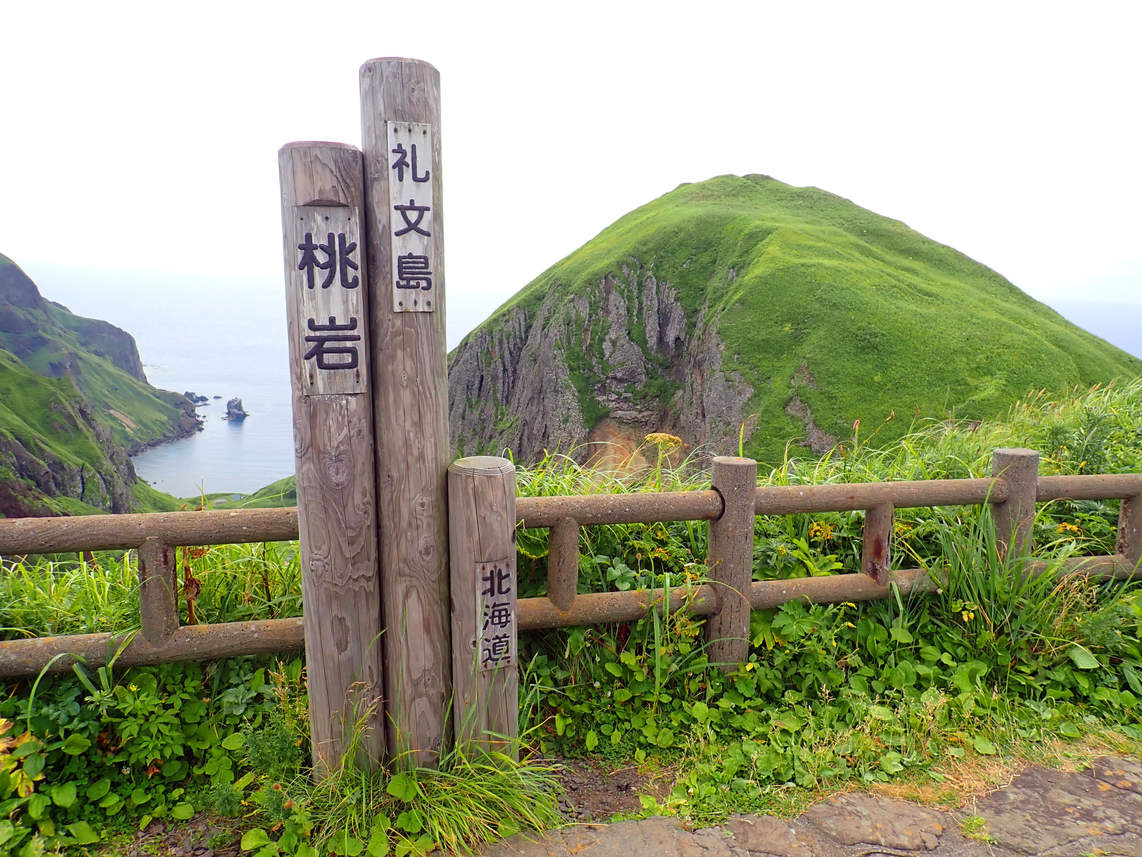 A wooden signpost with Chinese characters, a coastal landscape, and a wooden fence.