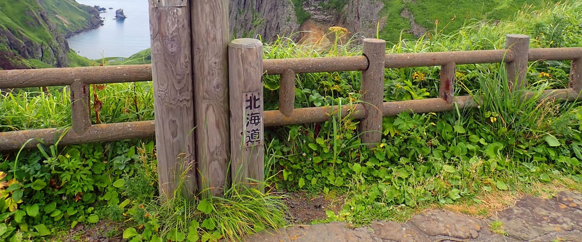 A wooden signpost with Chinese characters, a coastal landscape, and a wooden fence.