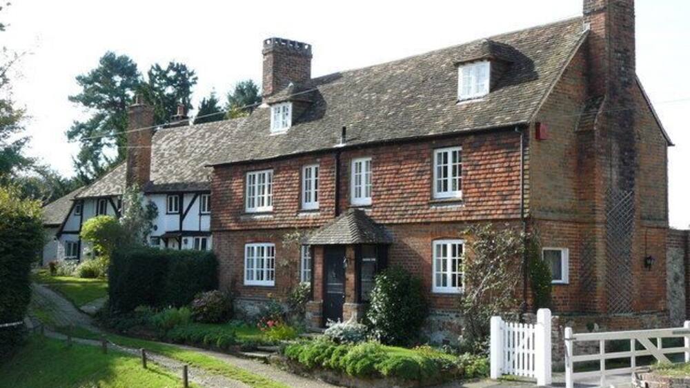 A traditional brick house with a white picket fence, surrounded by well-maintained gardens and a paved driveway.