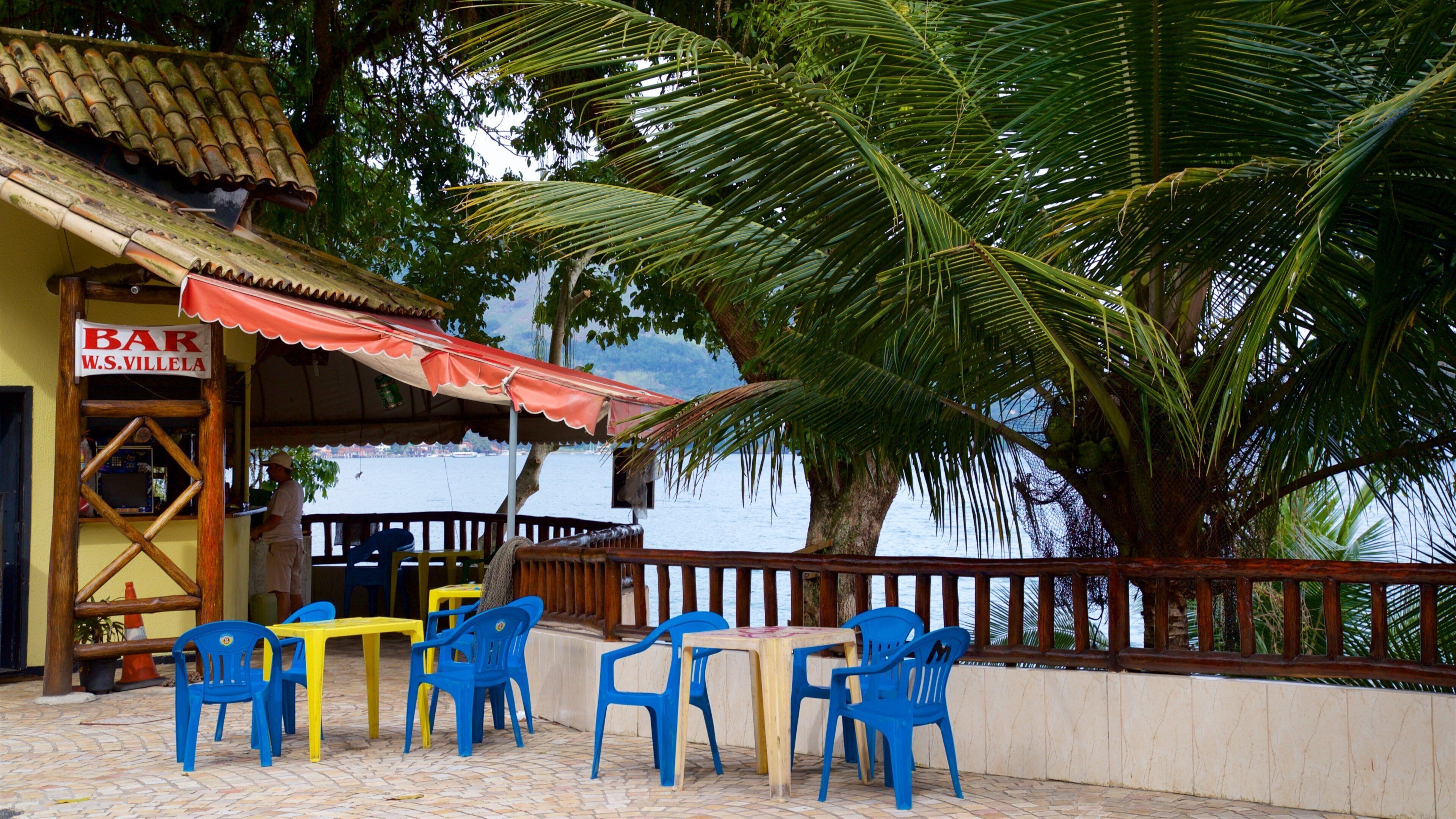 A beachside bar with outdoor seating and a palm tree.
